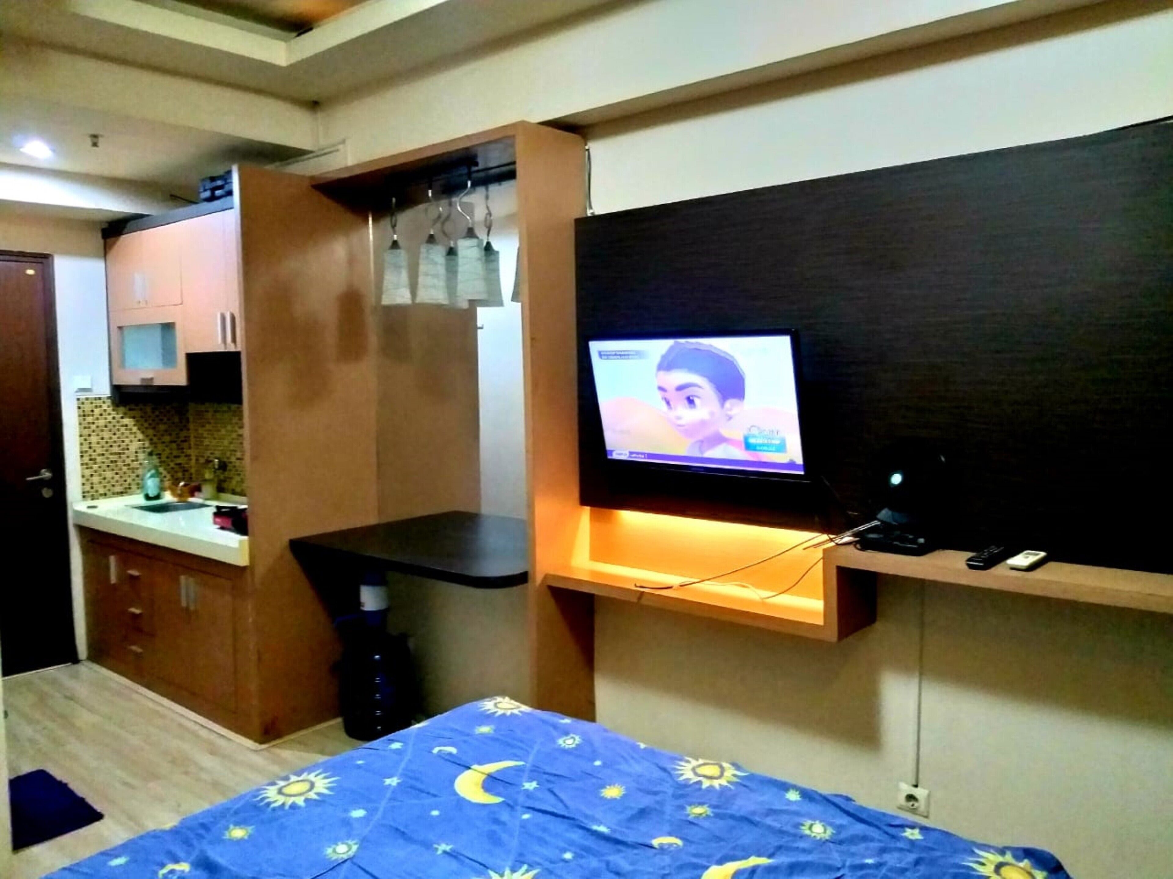 Een compacte kamer met een bed, een aan de muur bevestigde televisie, een kleine kitchenette en een kledingkast.