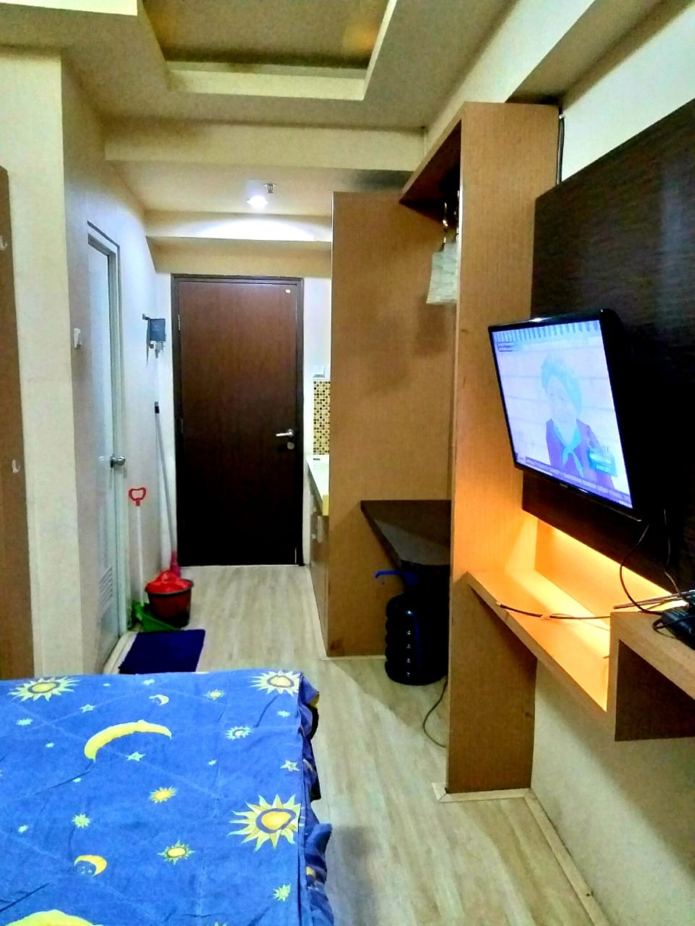A compact hotel room with a bed, a television on a stand, a desk, and a door leading to another room.