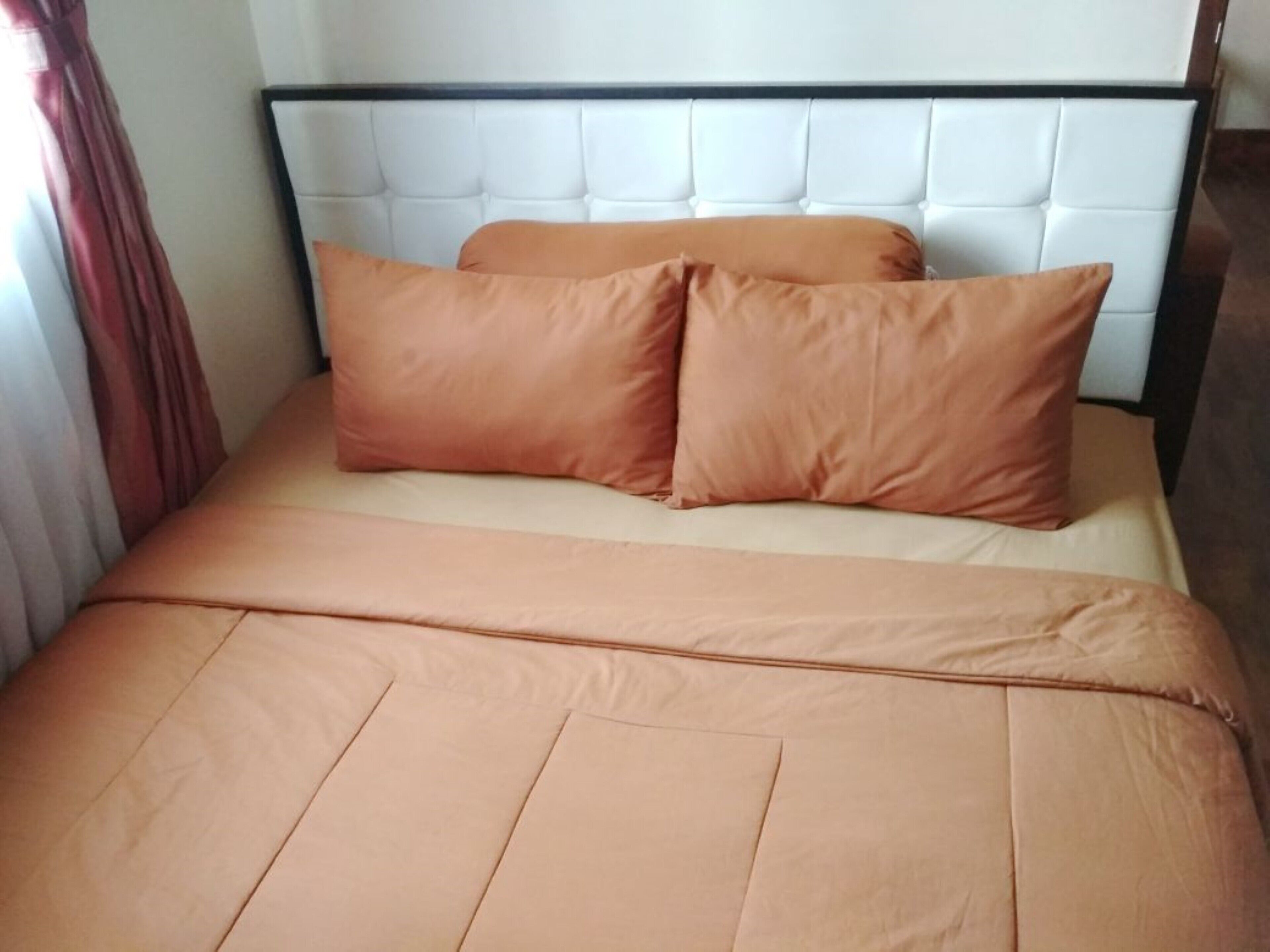 Un letto con una testiera bianca e due cuscini color pesca.