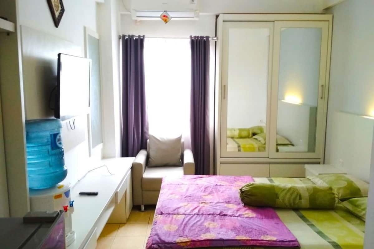 Habitación de hotel con cama, escritorio, silla, armario y una ventana grande con cortinas.