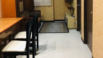 A compact room with a dining table and chairs, a small TV mounted on the wall, and a door leading to another room.