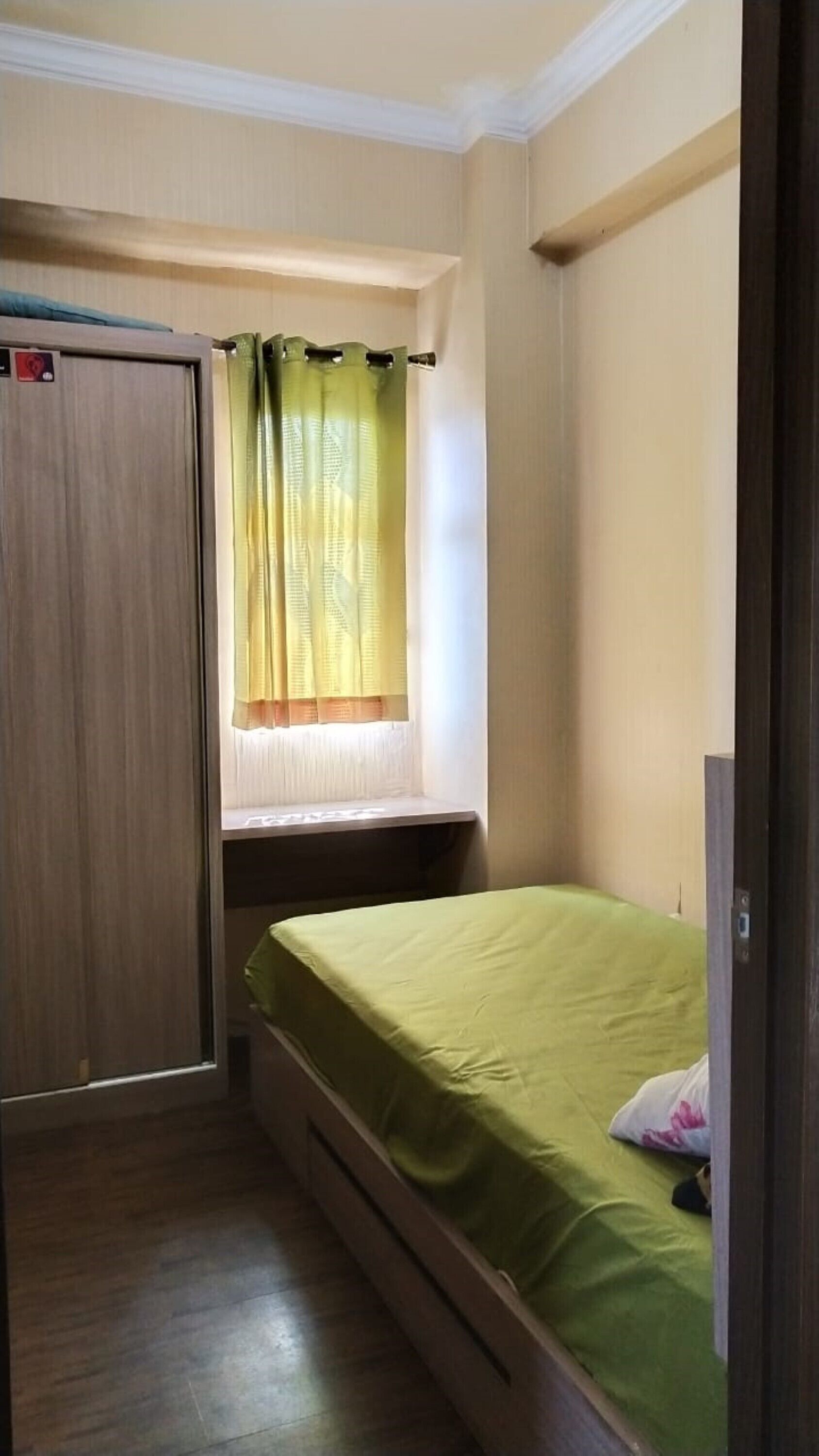 Une petite pièce avec un lit simple, une fenêtre avec des rideaux, une armoire en bois et une porte.