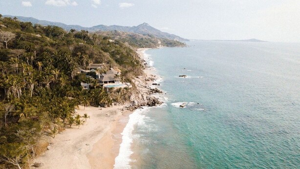 Uma propriedade costeira com praia, montanhas ao fundo e vista ampla para o oceano.