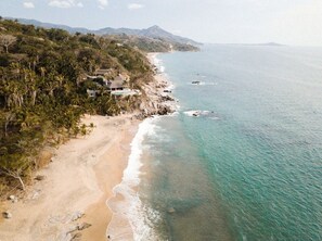Une propriété située sur la côte, avec une plage, un paysage montagneux en arrière-plan et une vue dégagée sur l’océan.