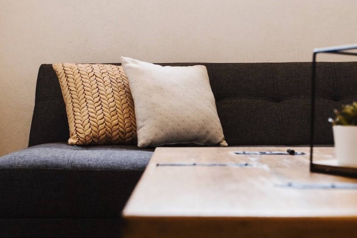 Ein dunkelgraues Sofa mit zwei Kissen, eines mit Zopfmuster und das andere schlicht, und ein kleiner Holztisch mit einer Pflanze.