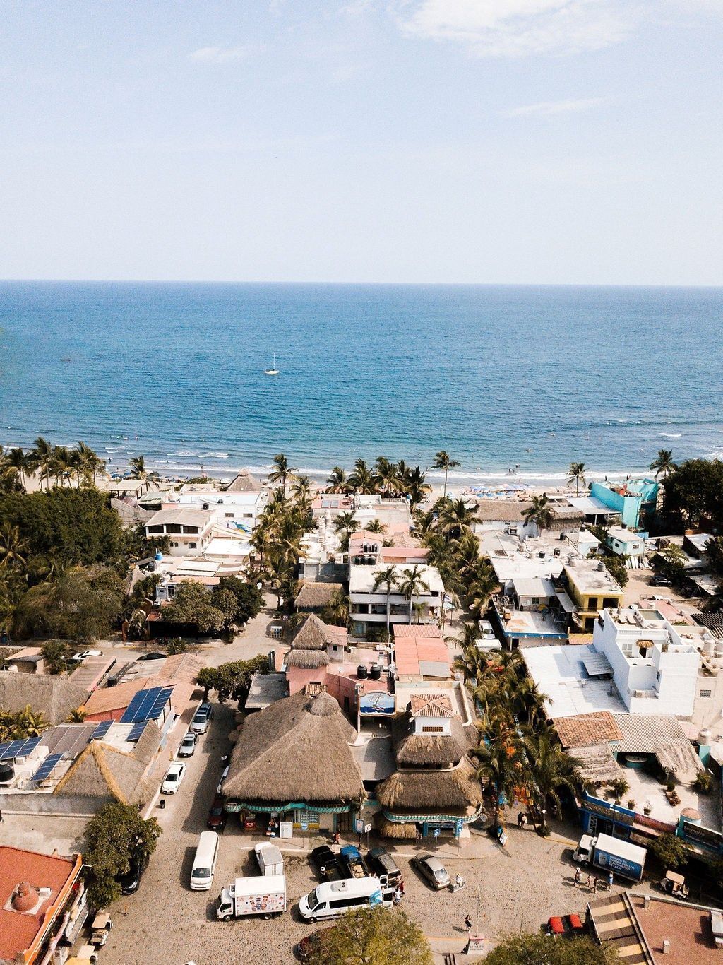 A coastal town with thatched-roof buildings, a beach, and a clear view of the ocean.