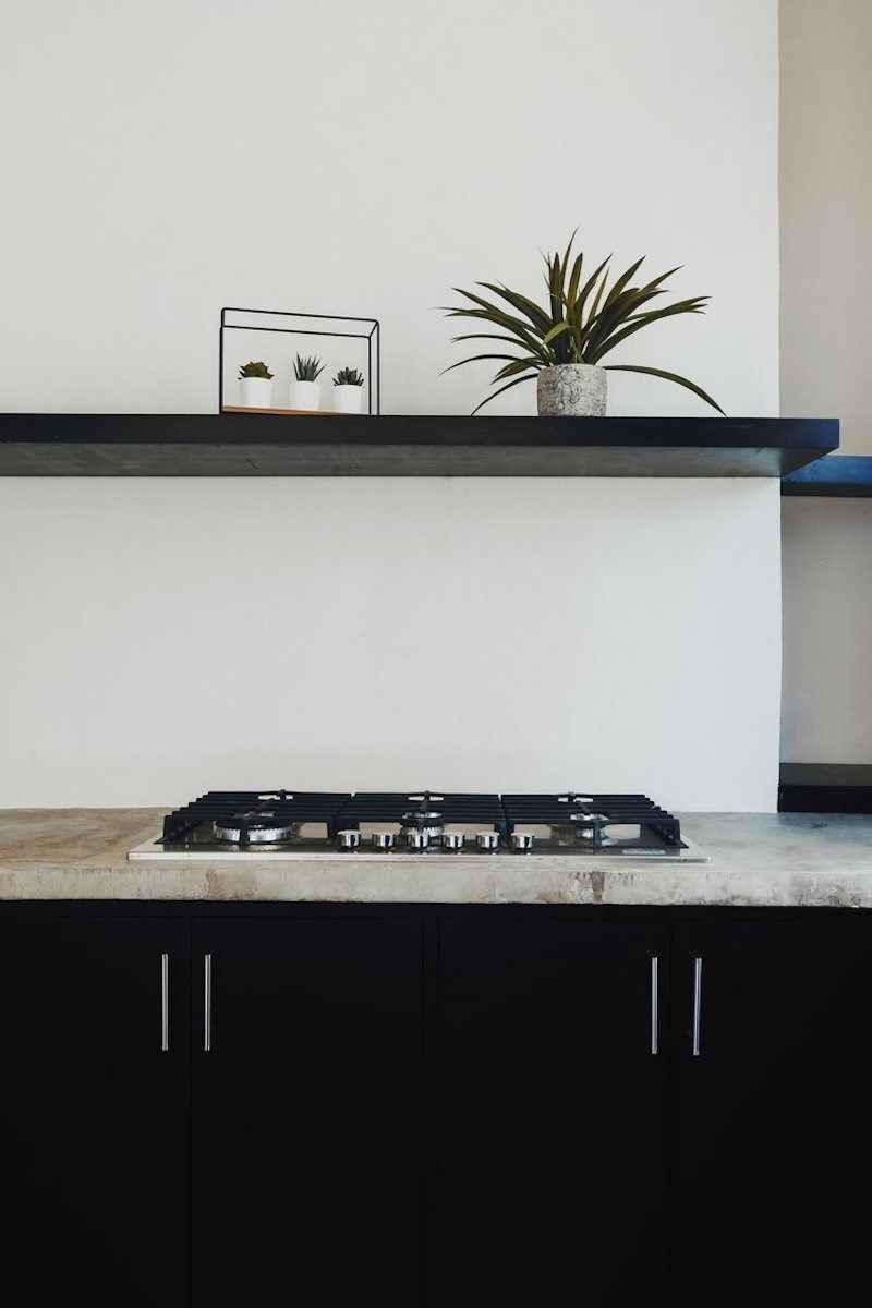 Una cocina con estufa a gas, armarios negros y encimera blanca.