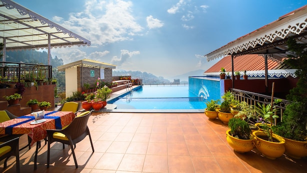 A rooftop pool area with a clear view of the mountains, surrounded by potted plants and outdoor seating.