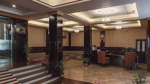 A lobby with a reception desk, seating area, and a staircase leading to an elevator.