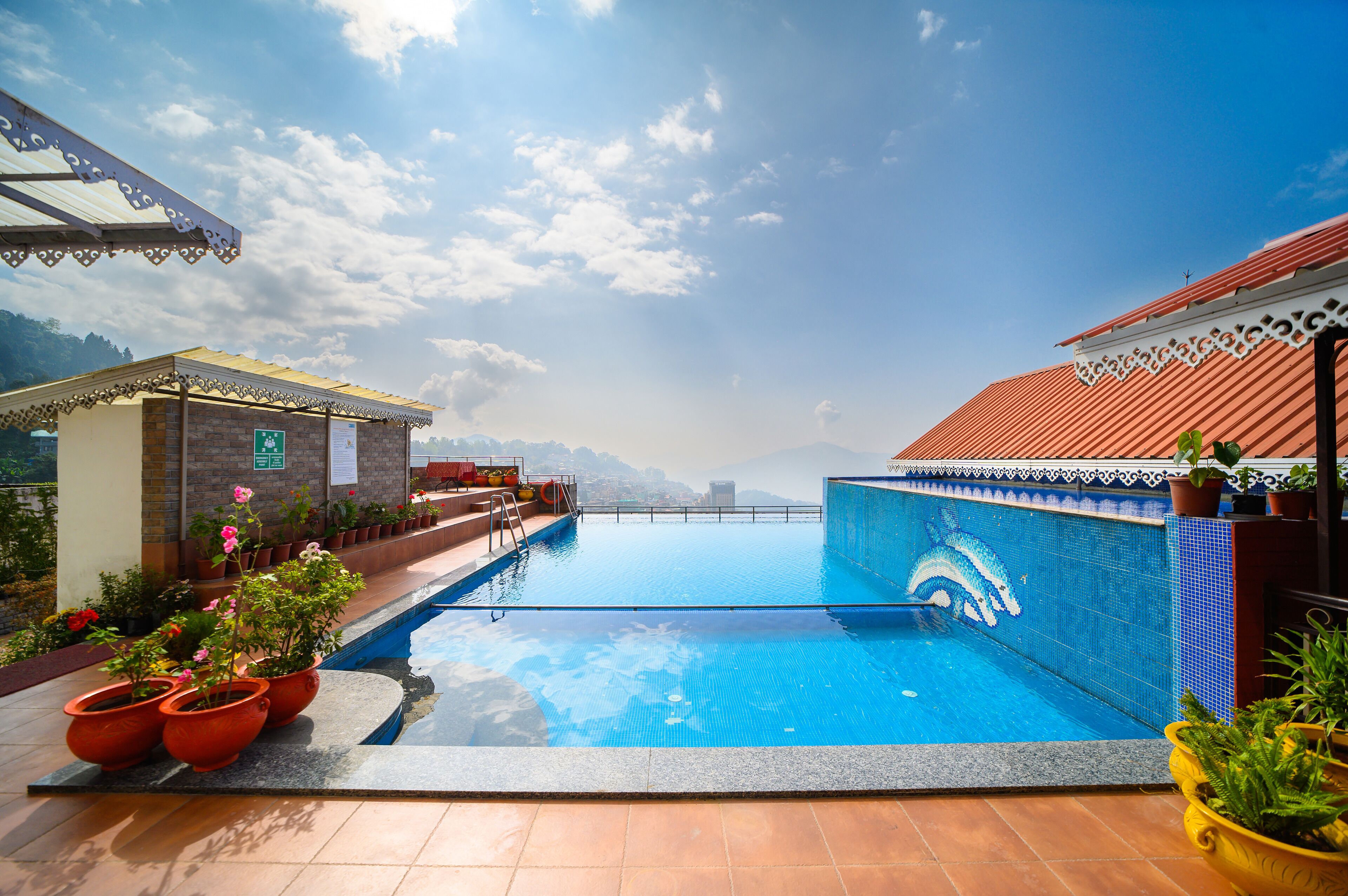 A swimming pool with a clear view of the mountains in the background, surrounded by potted plants and a covered seating area.