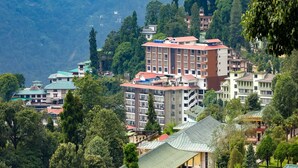 A multi-story hotel with a red roof, surrounded by lush greenery and mountains in the background.