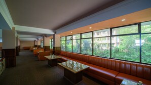 A spacious lobby with a long orange leather bench, a glass-top coffee table, and a view of greenery through large windows.