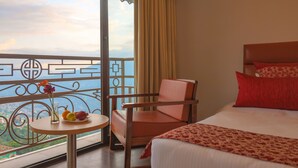 A hotel room with a bed, a chair, a small table with fruit, and a balcony with a view.