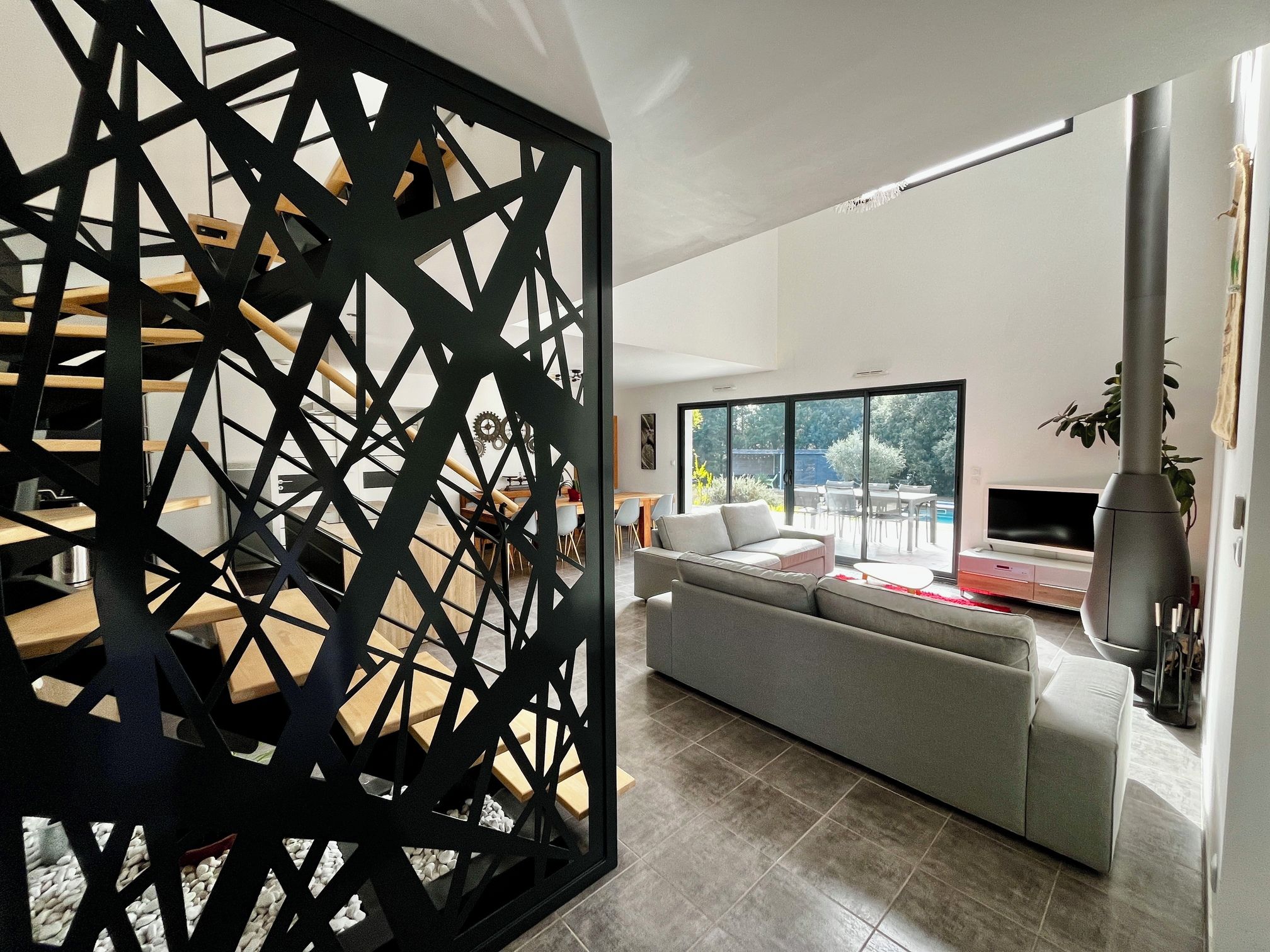 Un salon moderne avec un canapé d’angle, un coin repas doté d’une table en bois et une grande fenêtre offrant une vue sur l’extérieur.