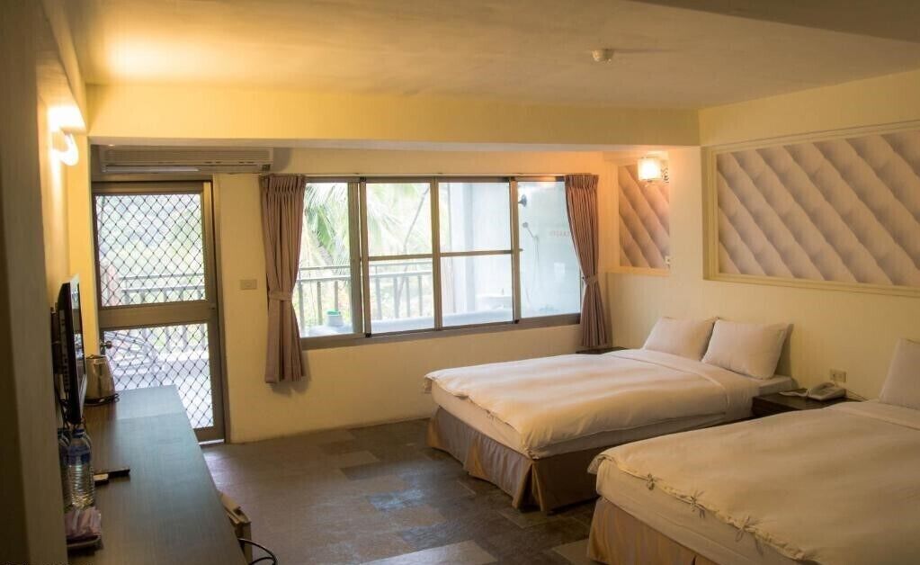 A hotel room with two beds, a small desk, a chair, and a window with curtains.
