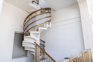 Eine Wendeltreppe mit hölzernem Geländer und weißen Stufen, die zu einer oberen Etage führt.