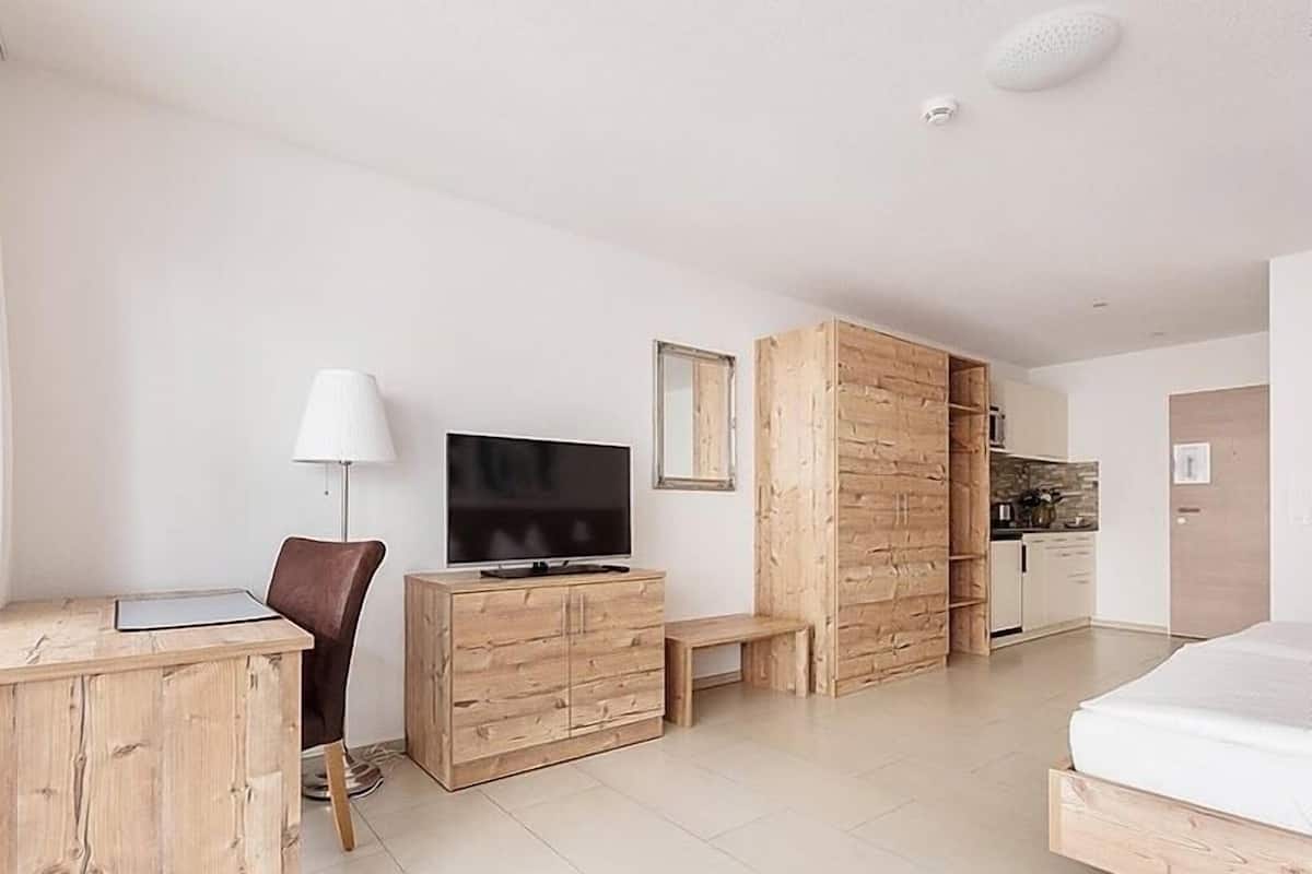 Quarto moderno com escrivaninha de madeira, televisão, um banco e uma cama.