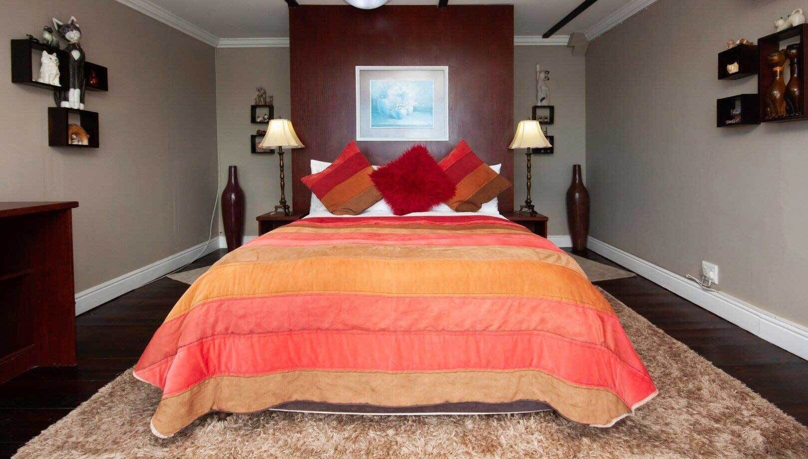 A bedroom with a large bed, two bedside tables, a wall-mounted shelf with decorative items, and a framed picture above the bed.