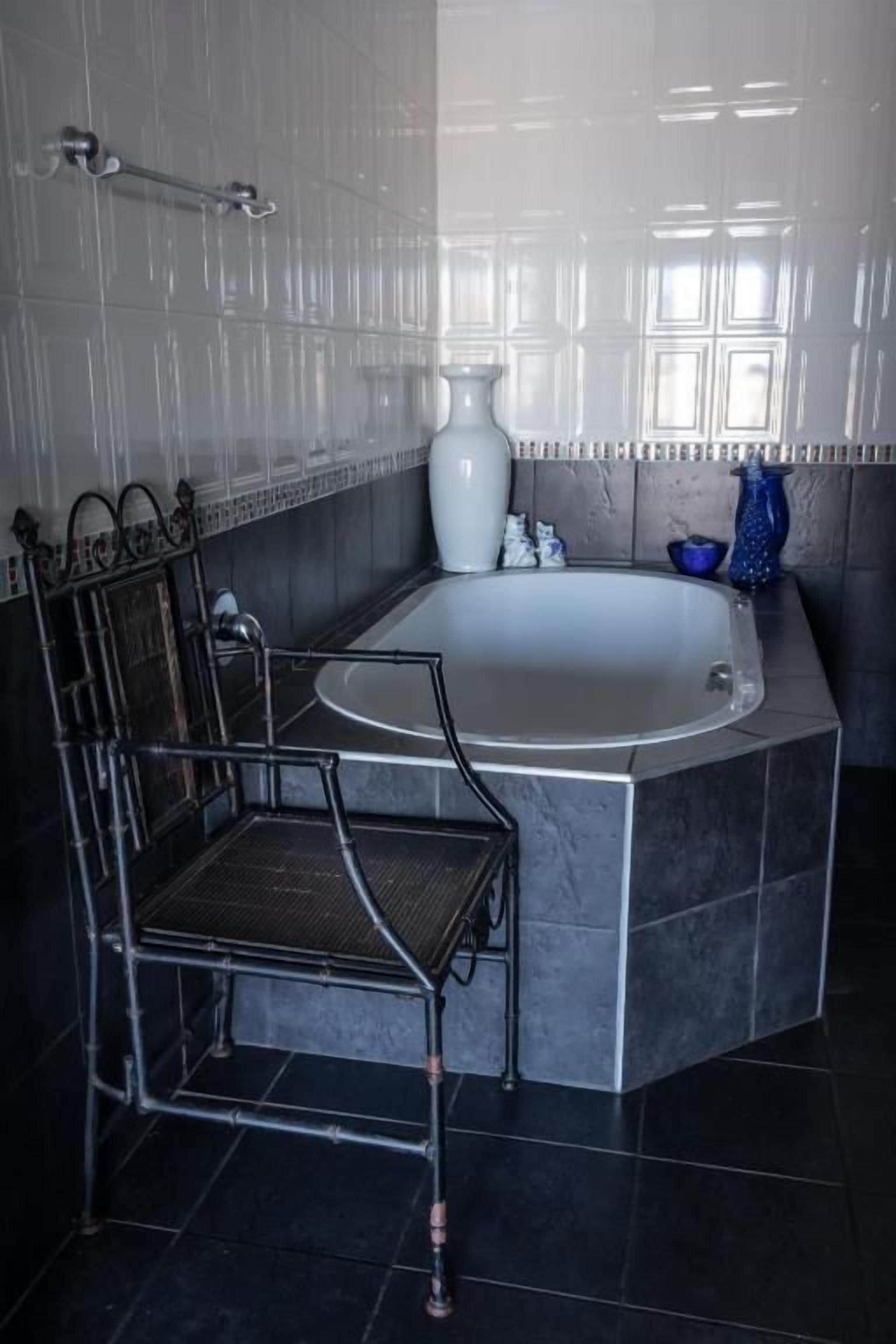 Un baño con bañera, una silla y un florero.