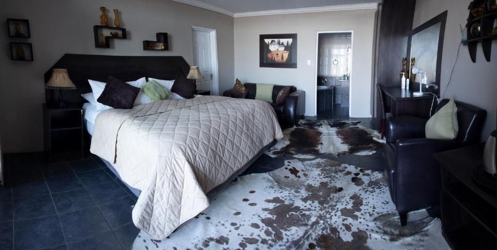 A bedroom with a large bed, a leather sofa, a cowhide rug, and a dining area in the background.
