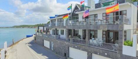 A multi-story hotel with balconies, flags, and a view of the sea.