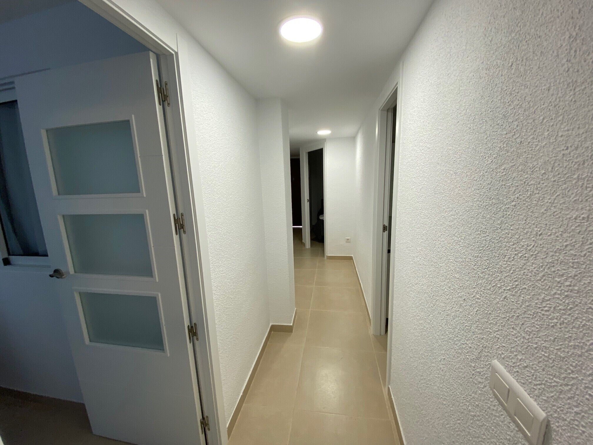 Un pasillo con paredes blancas y piso de baldosas, que conduce a una puerta al final.