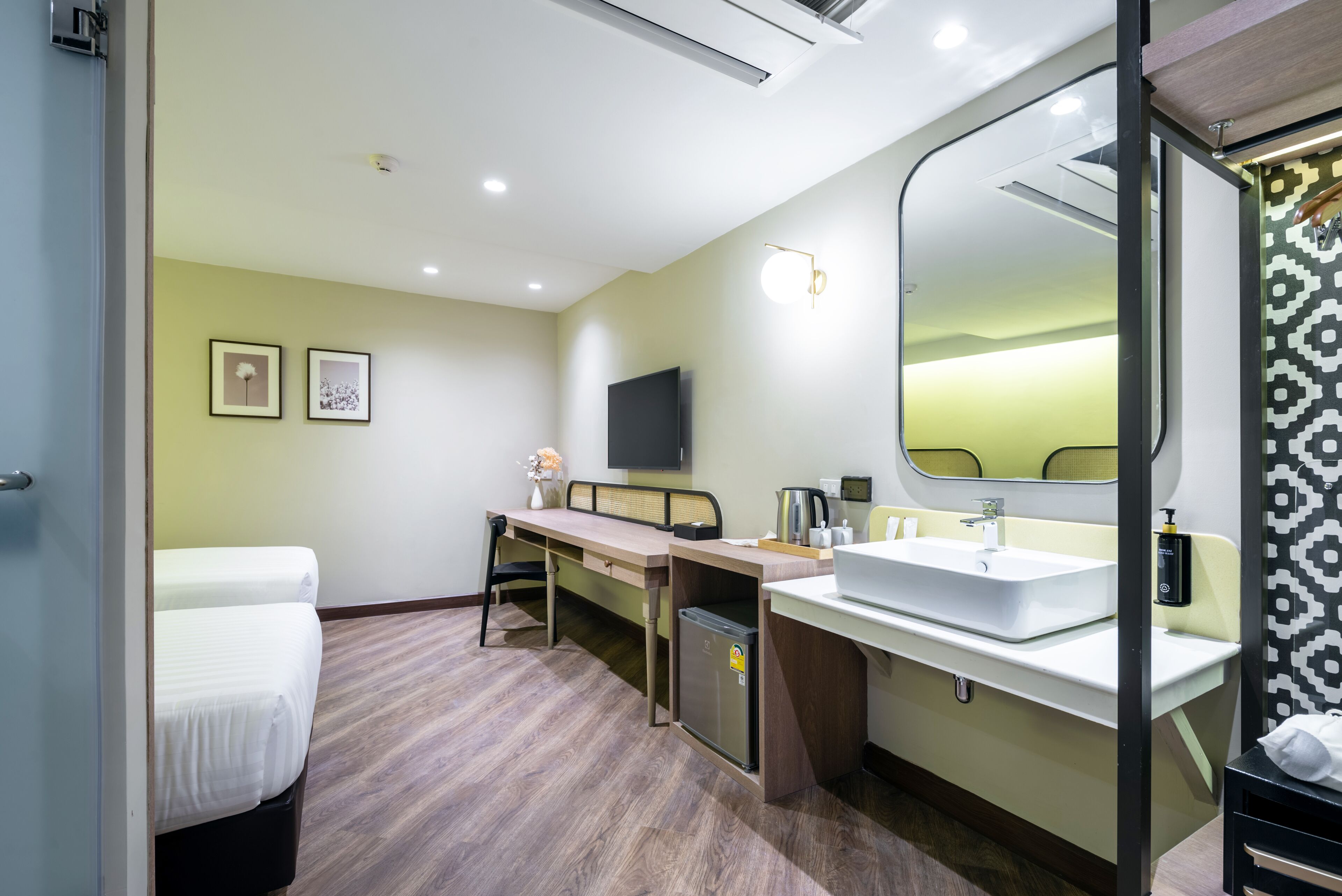 A modern hotel room with a bed, a desk, a large mirror, a sink, and a television.