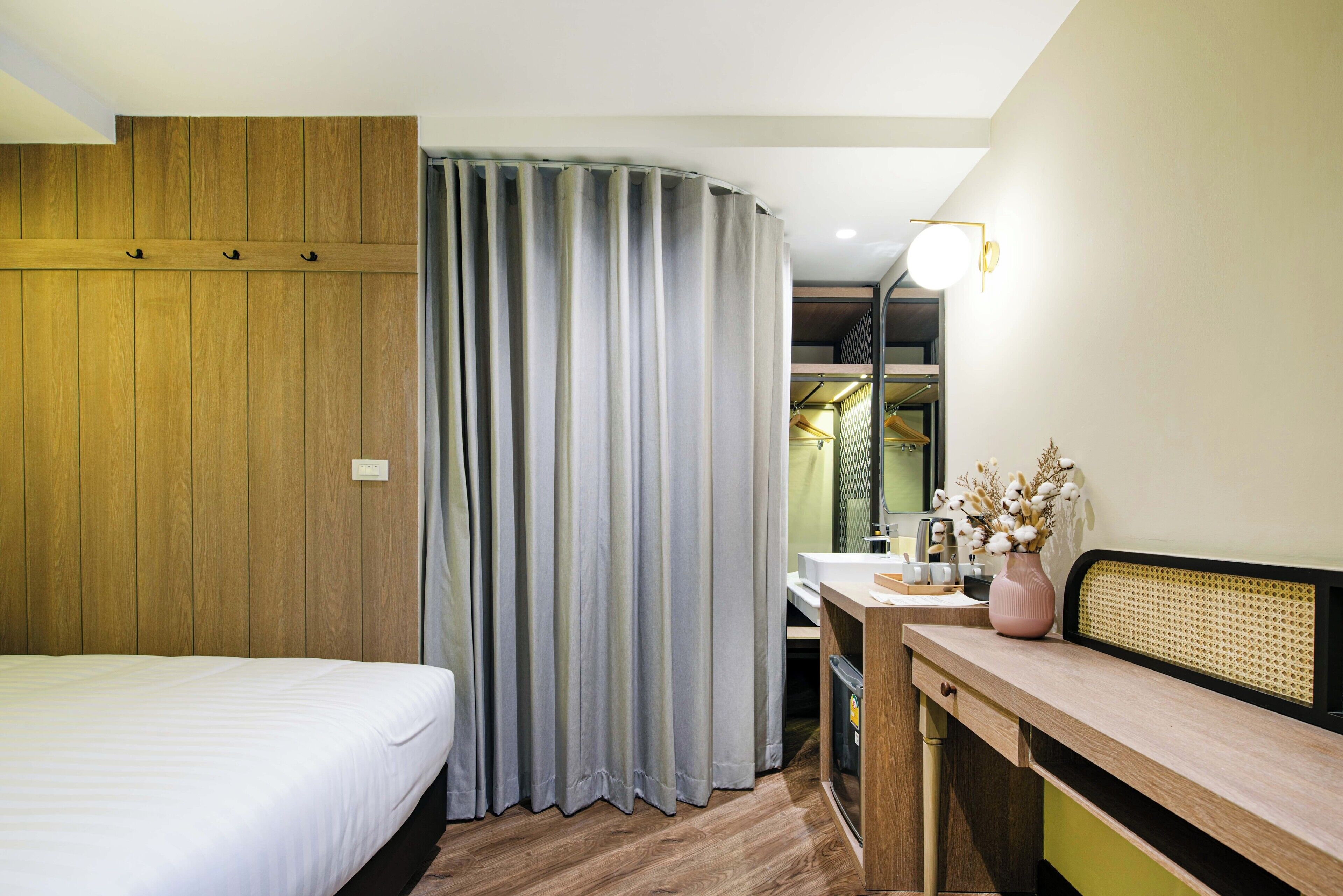 A hotel room with a bed, a desk, a chair, a mirror, and a curtain.