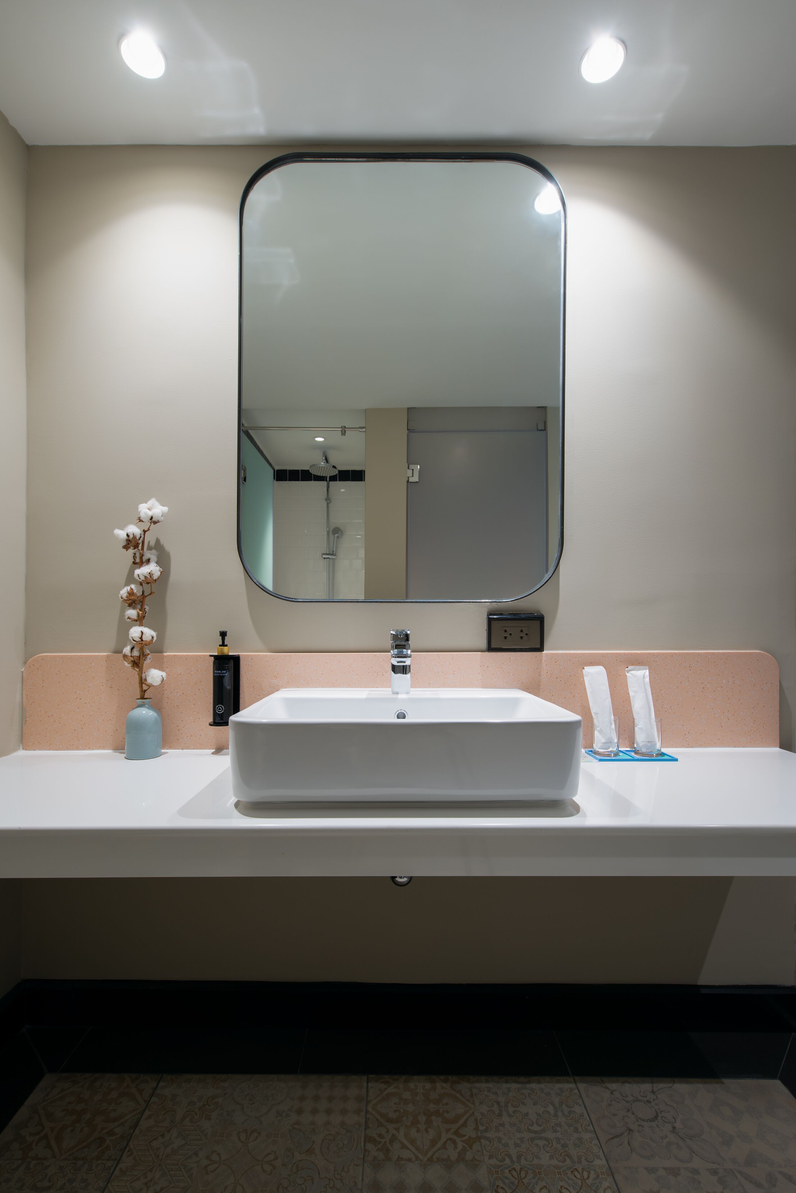 A bathroom with a white sink, a large mirror, and a vase with flowers.