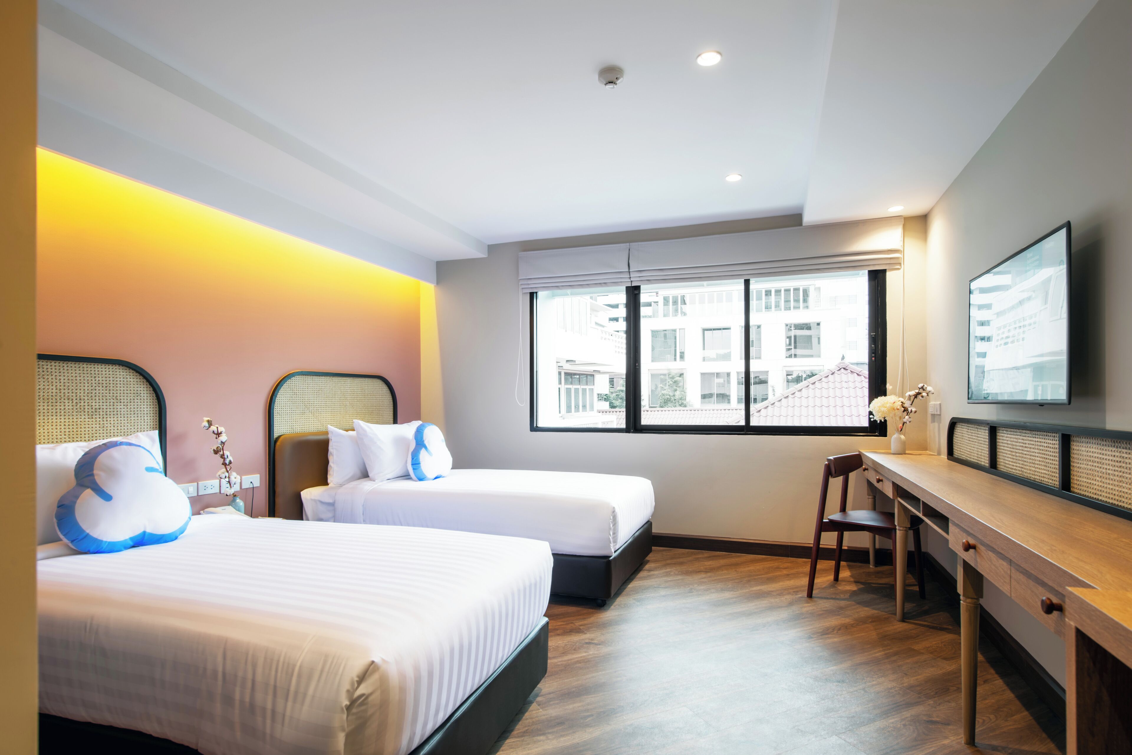 Habitación de hotel con dos camas, un escritorio y un amplio ventanal con vistas a la ciudad.