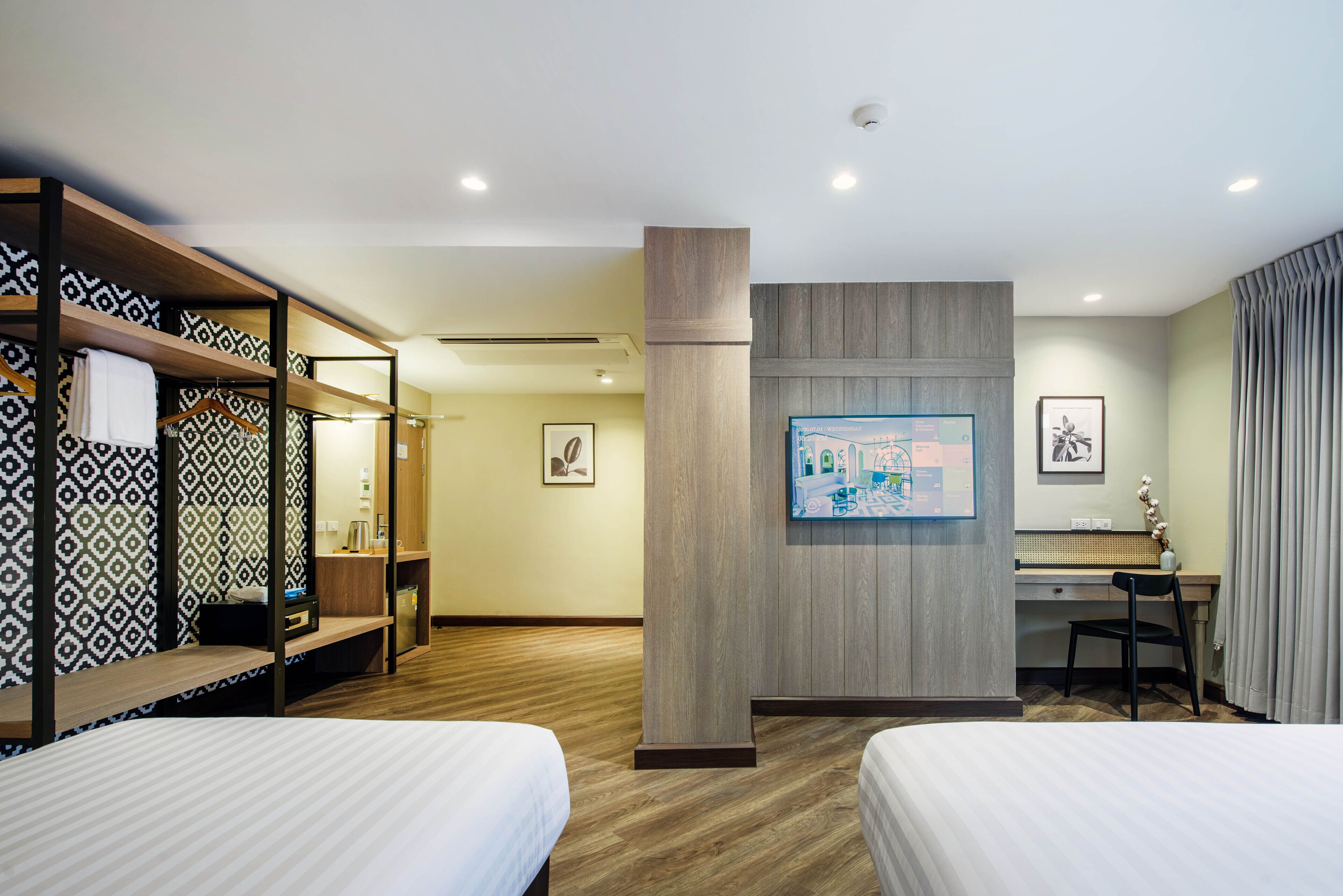 A hotel room with two beds, a desk, a chair, a wardrobe, and a wall-mounted TV.