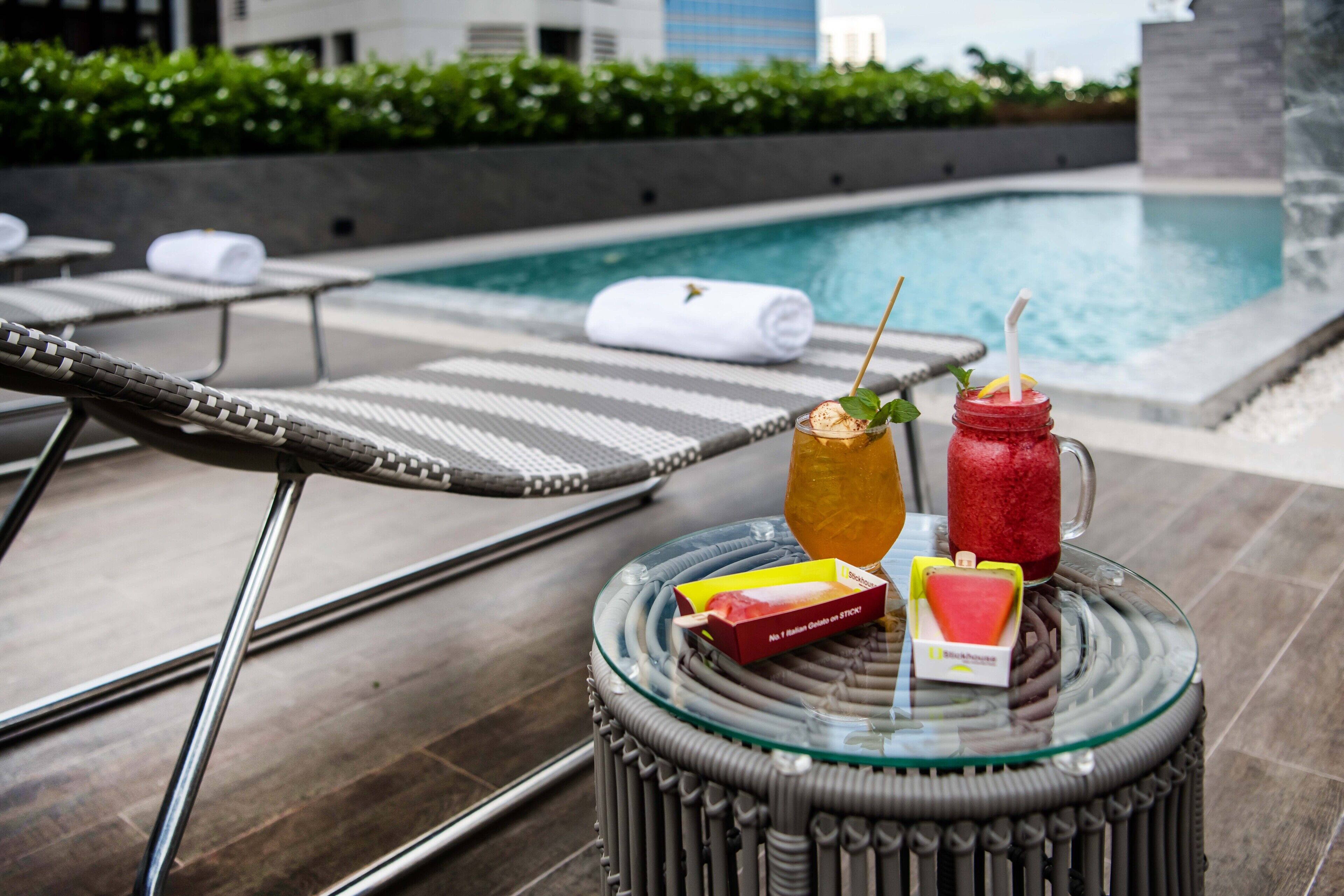 A poolside area with lounge chairs, a glass table with drinks and snacks, and a view of the pool.