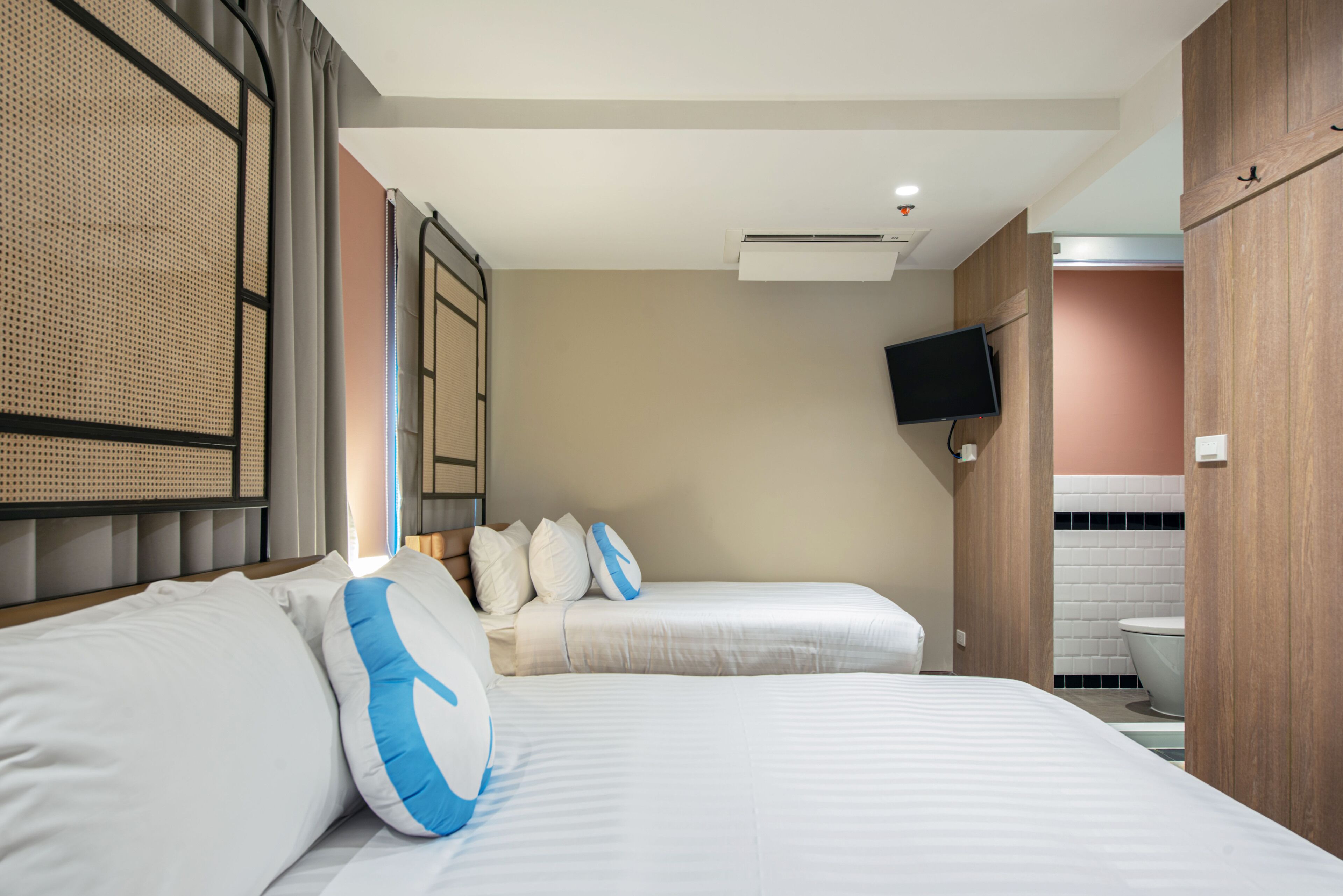 A hotel room with two beds, a television mounted on the wall, and a bathroom visible through an open door.