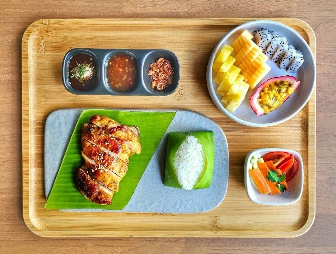A meal tray with grilled chicken, rice, and various side dishes including fruit and vegetables.