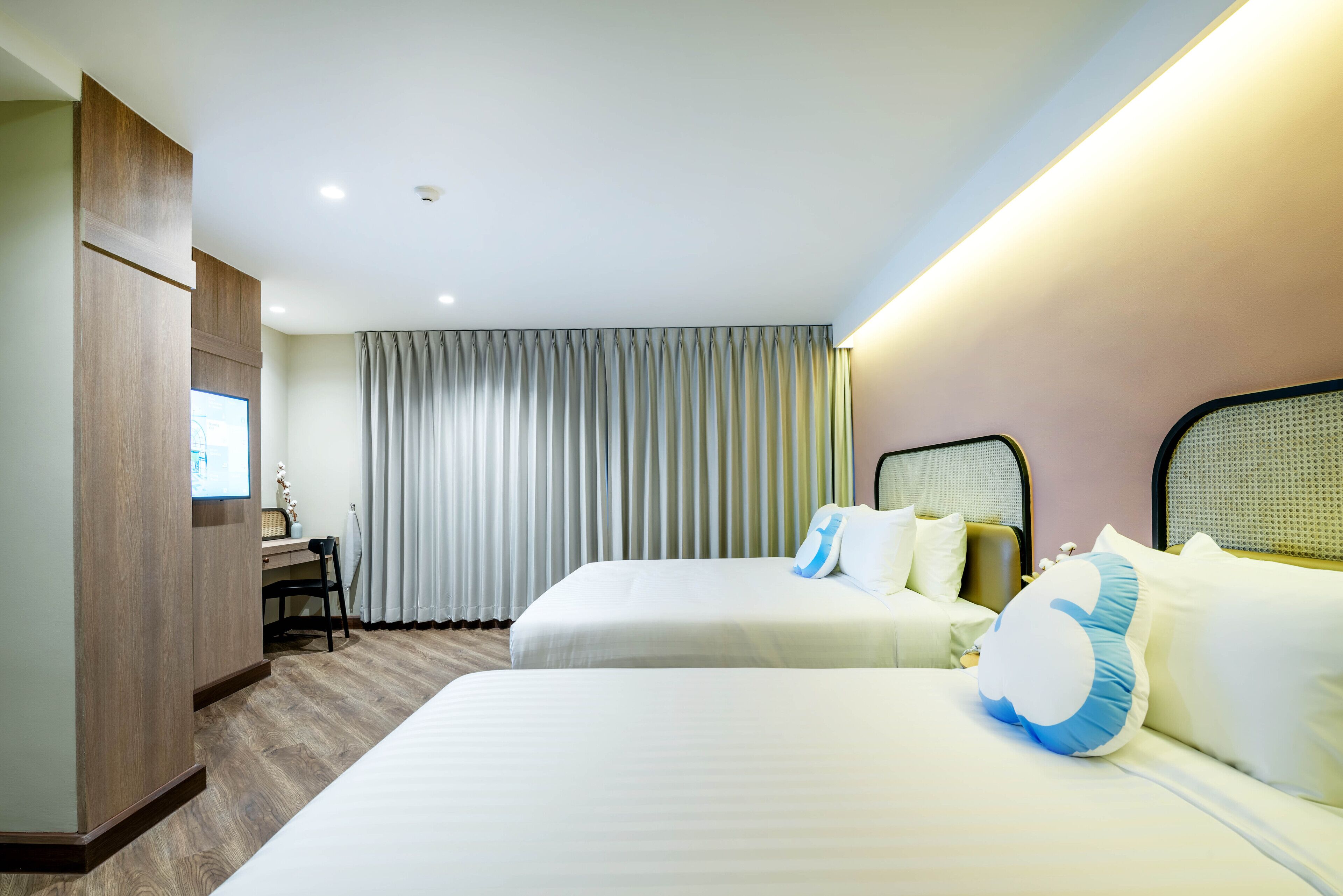 A hotel room with two beds, a desk, and a large window with curtains.