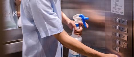 A person in a light blue shirt inside an elevator, holding a spray bottle.