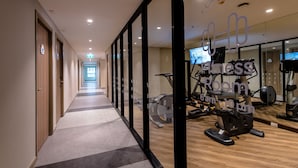 Een sportschool met trainingsapparatuur, een spiegelwand en een gang met deuren.