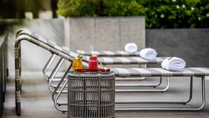 Een modern buitenzitje met metalen stoelen en een rieten tafel waarop twee drankjes staan.