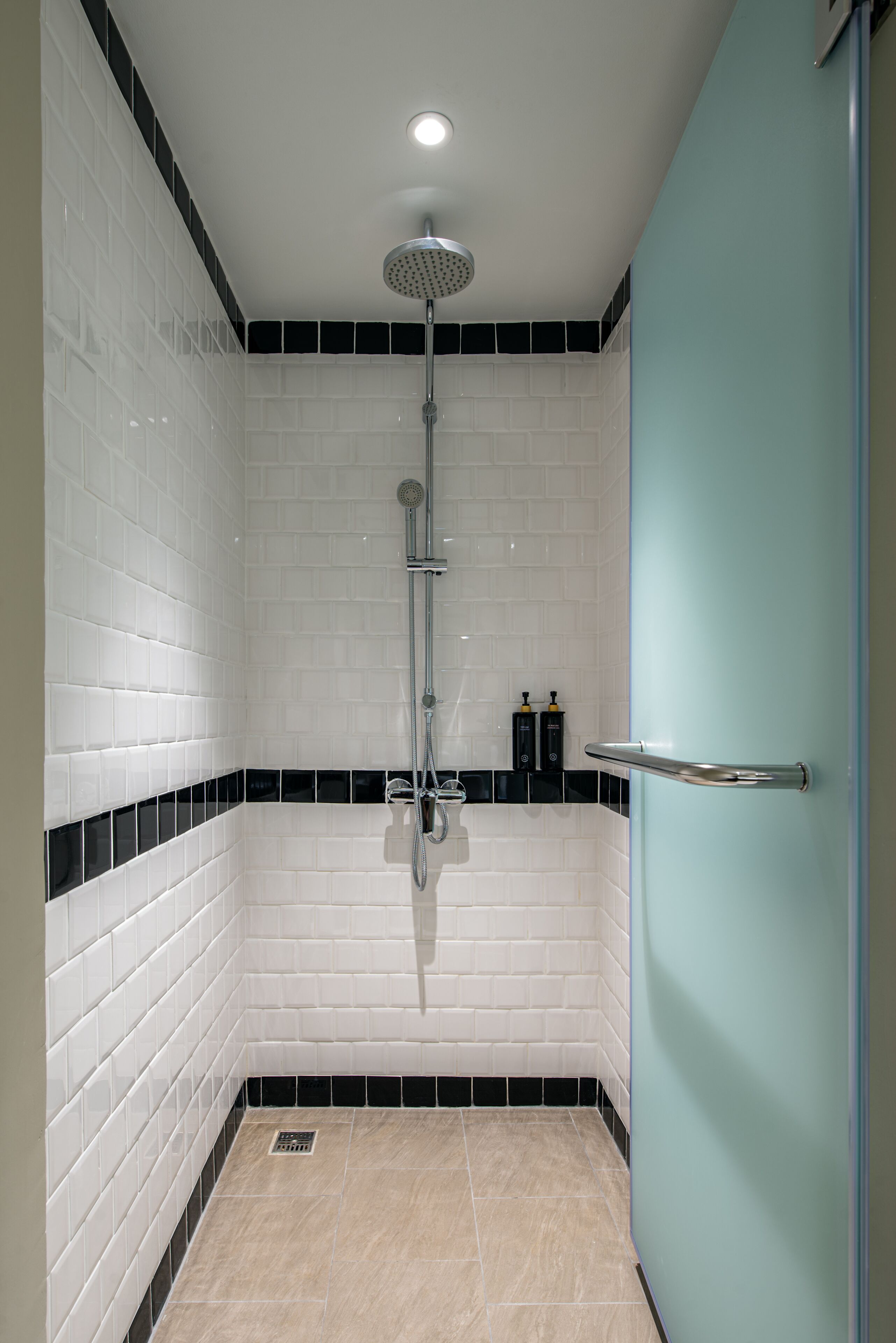 Un baño con azulejos blancos tipo metro, un detalle en blanco y negro, un cabezal de ducha y una barra de apoyo.