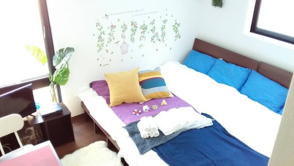 Una cama bien hecha con almohadas azules y amarillas, una manta blanca y una mesita de noche con una lámpara.