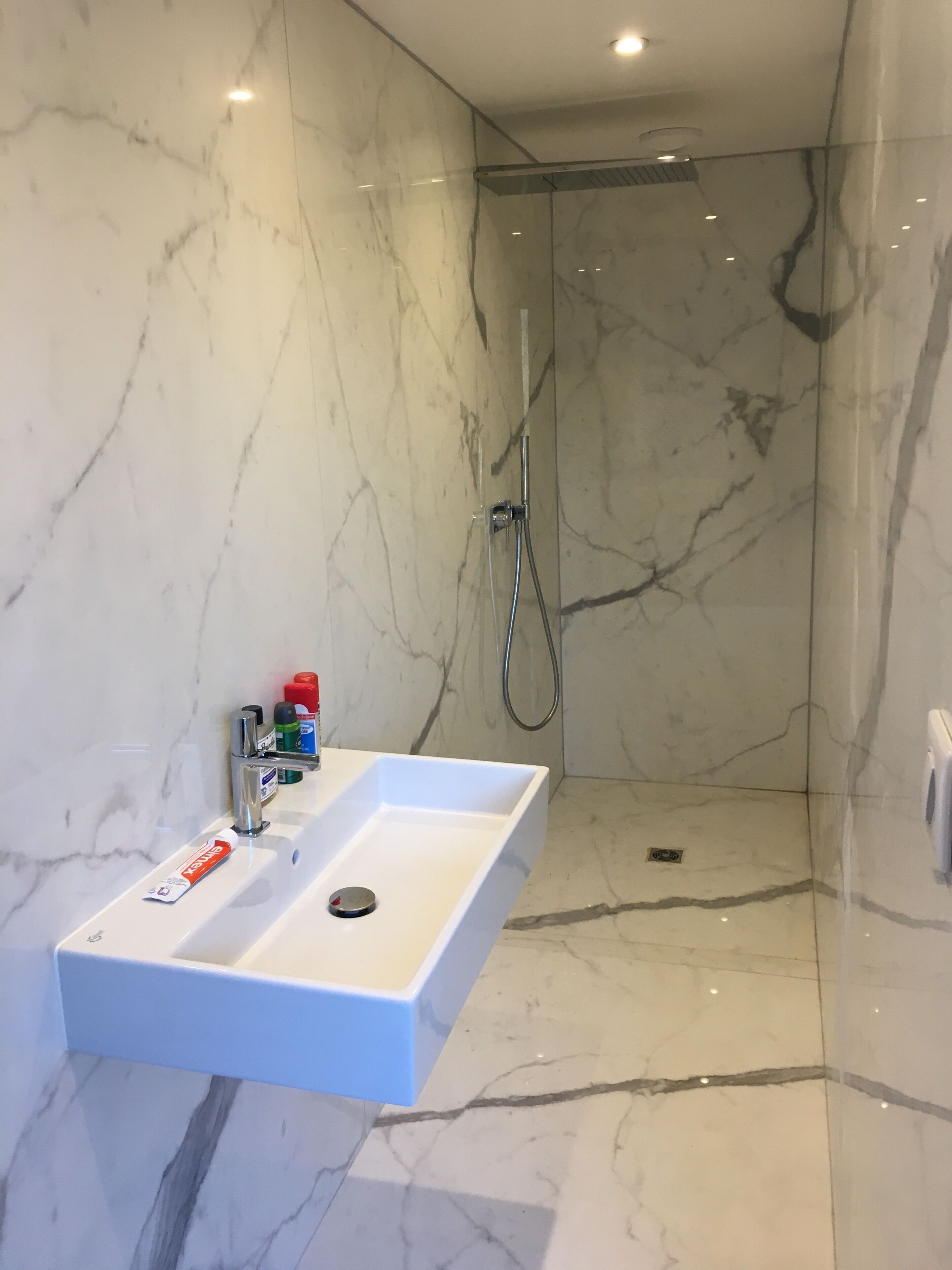 A bathroom with a white marble sink, a handheld showerhead, and a marble floor.