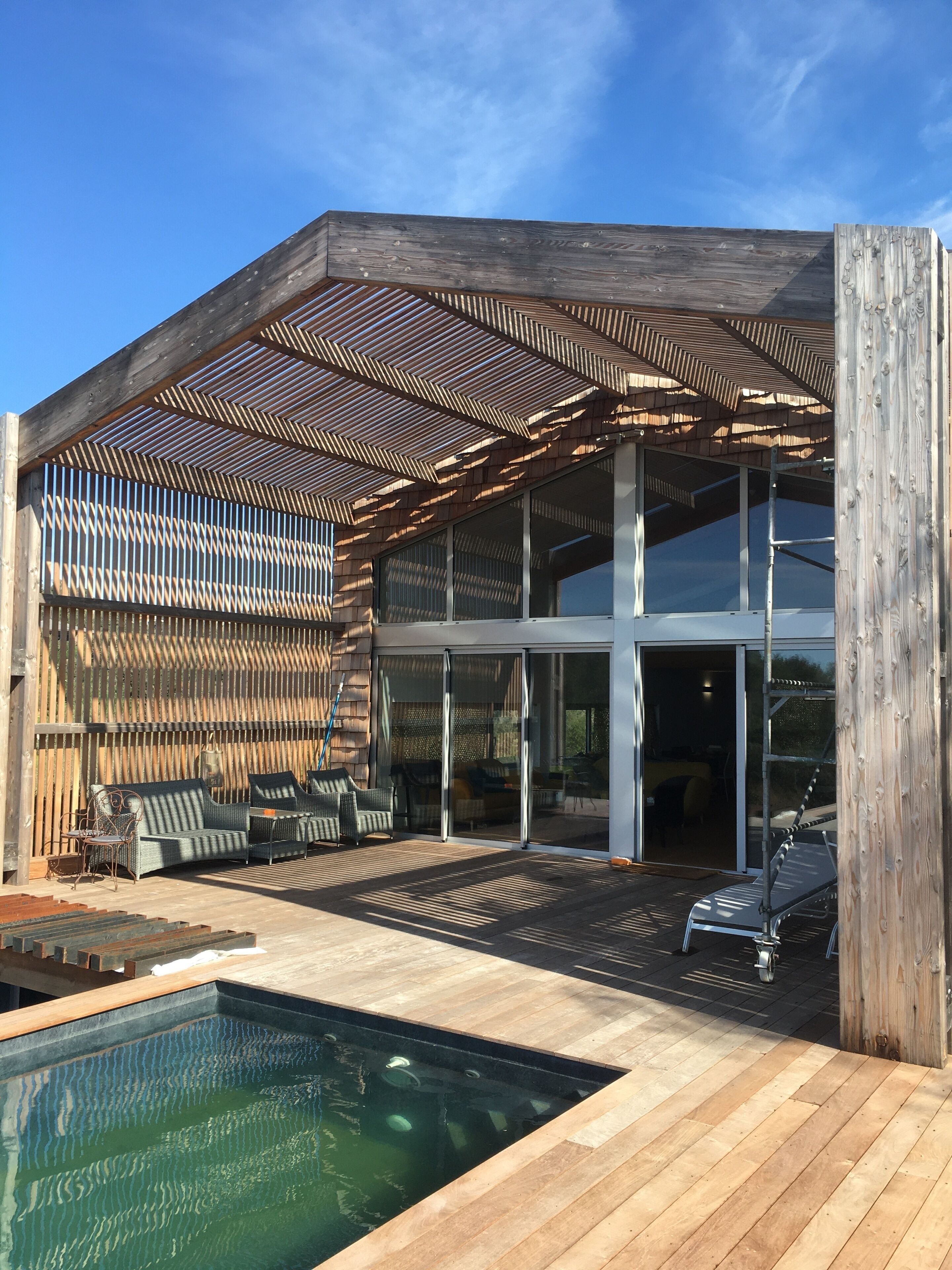 A modern house with a pool, outdoor seating, and a covered patio area.