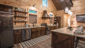 A spacious kitchen with wooden walls, a large island, stainless steel appliances, and a hanging light fixture.