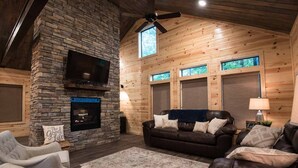 A cozy living room with a stone fireplace, leather sofas, and a ceiling fan.