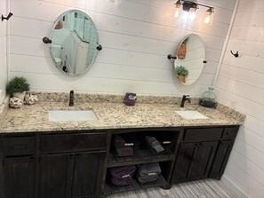 A bathroom with a granite countertop, two sinks, dark wooden cabinets, and a mirror with a pinecone decoration.