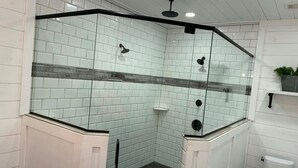 A corner bathroom with white tiled walls, a glass shower enclosure, a black tiled floor, and a white toilet.