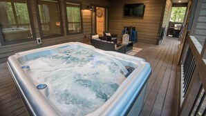 A hot tub in a wooden deck area with a clock on the wall and a seating area with a table and chairs.
