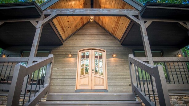 A wooden cabin with a central door, a staircase leading up to it, and a roof with a triangular peak.