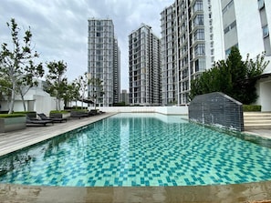 A swimming pool with a checkered pattern, surrounded by modern buildings and lounge chairs. - Paragon Cyberjaya by Elite Stay (Cyberjaya)