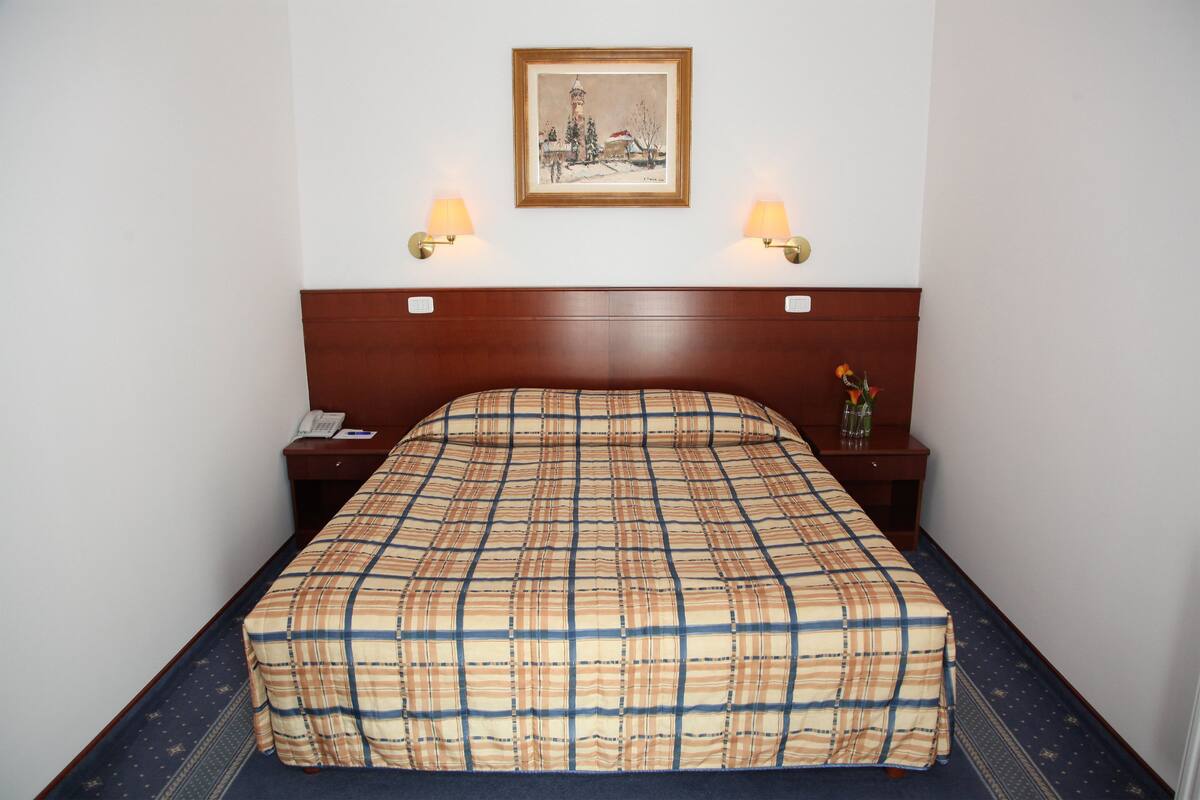 A hotel room with a bed, two bedside lamps, a nightstand, a telephone, and a framed picture on the wall.